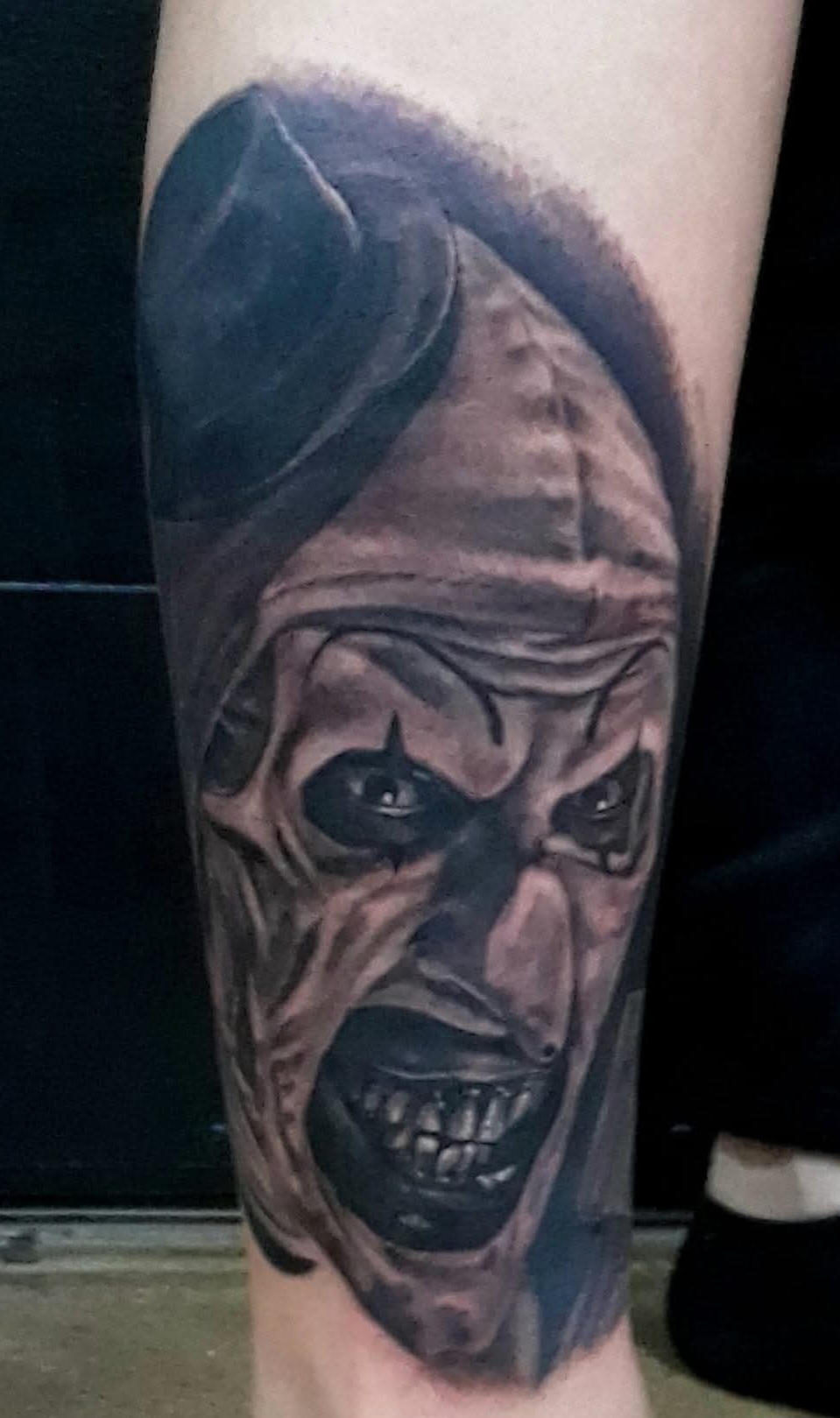 Black-and-grey evil jester portrait tattoo on forearm